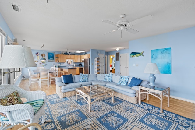 living room with ceiling fan, a textured ceiling, and light hardwood / wood-style floors