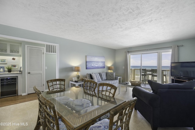 dining space with bar, light tile patterned floors, beverage cooler, and a textured ceiling