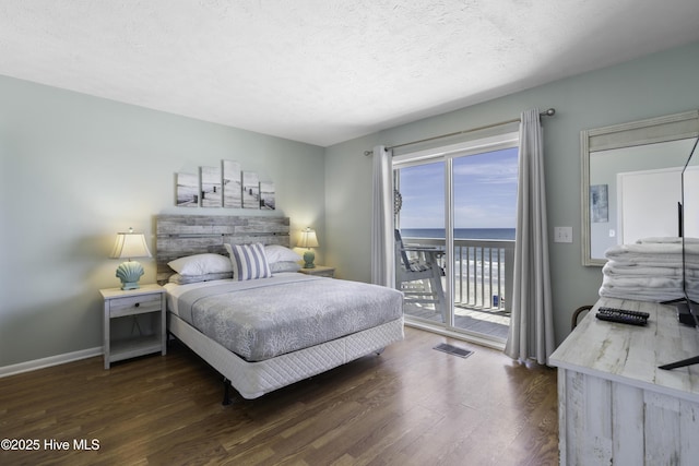 bedroom with dark hardwood / wood-style flooring, access to exterior, a textured ceiling, and a water view