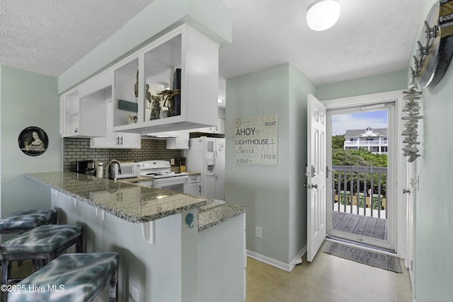 kitchen featuring white appliances, kitchen peninsula, white cabinets, and stone countertops