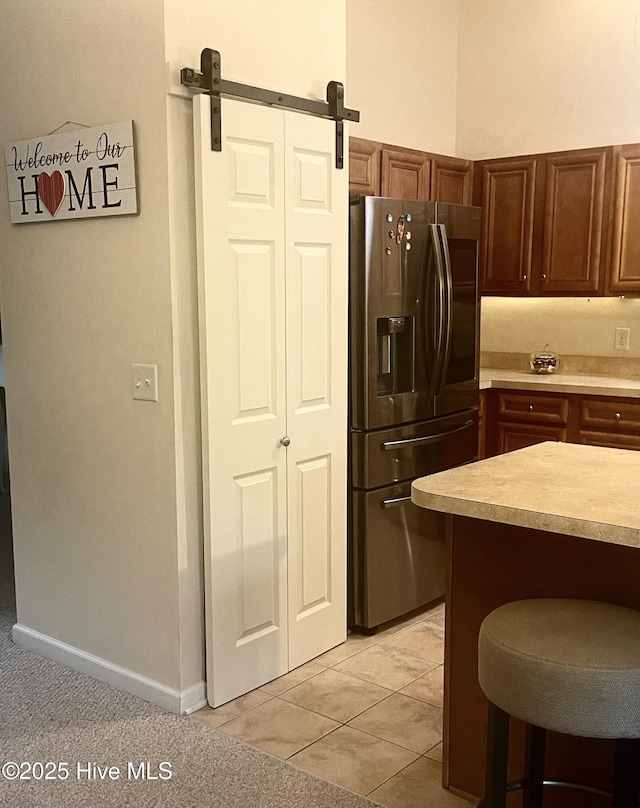 kitchen featuring stainless steel fridge, a barn door, baseboards, light countertops, and light tile patterned flooring