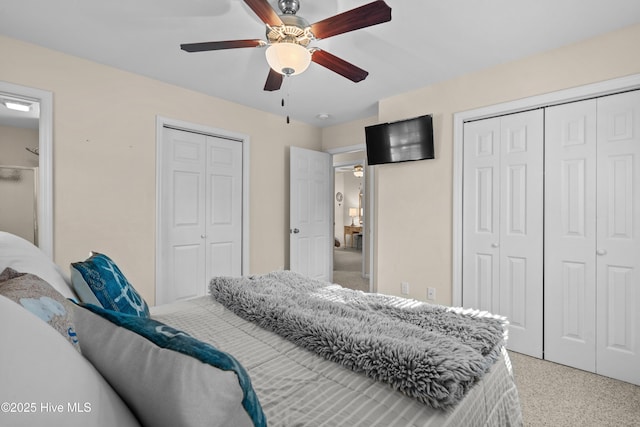 bedroom featuring light colored carpet, ceiling fan, and two closets