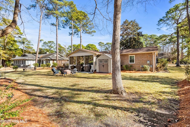 back of house with an outdoor fire pit, brick siding, a lawn, and a storage shed