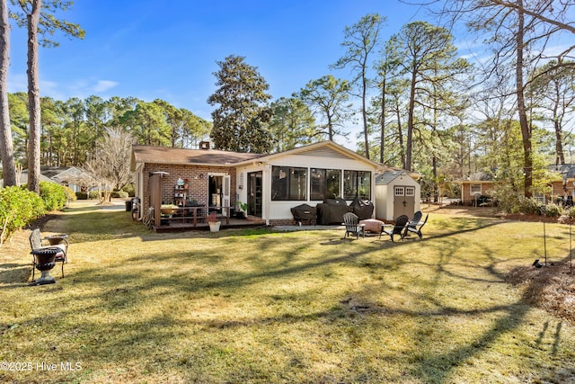 back of house with a yard, an outdoor fire pit, a sunroom, and brick siding