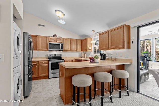 kitchen featuring a peninsula, stacked washer / drying machine, light countertops, appliances with stainless steel finishes, and hanging light fixtures