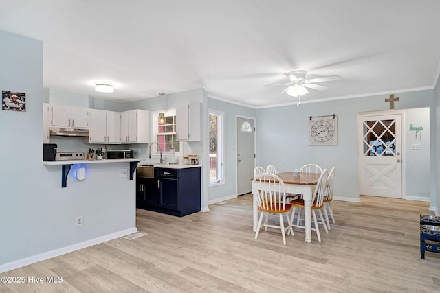 kitchen with sink, light hardwood / wood-style flooring, white cabinets, a kitchen bar, and decorative light fixtures