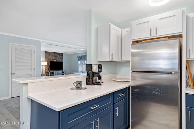 kitchen featuring stainless steel refrigerator, white cabinets, light stone countertops, blue cabinetry, and light wood-type flooring