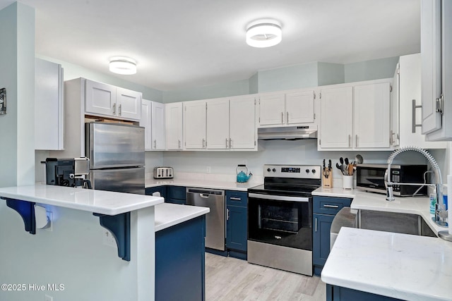 kitchen with blue cabinets, a breakfast bar, white cabinetry, light hardwood / wood-style flooring, and appliances with stainless steel finishes