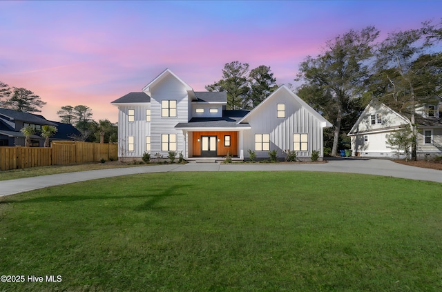 modern farmhouse featuring concrete driveway, board and batten siding, fence, and a lawn