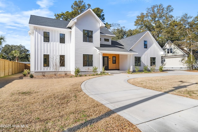 modern farmhouse style home with a shingled roof, board and batten siding, curved driveway, and fence