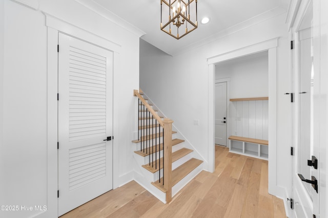 stairway with hardwood / wood-style flooring, crown molding, and an inviting chandelier