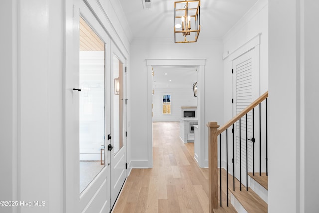 corridor featuring an inviting chandelier, ornamental molding, and light hardwood / wood-style flooring