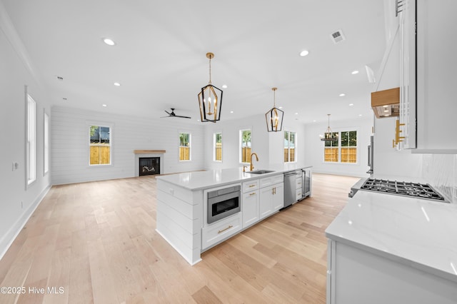 kitchen featuring sink, appliances with stainless steel finishes, white cabinetry, hanging light fixtures, and a center island with sink