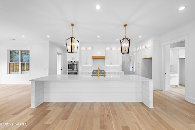 kitchen with a spacious island, premium range hood, sink, pendant lighting, and white cabinets