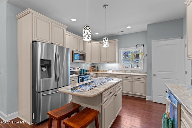 kitchen featuring a kitchen island, appliances with stainless steel finishes, pendant lighting, dark wood-type flooring, and cream cabinetry