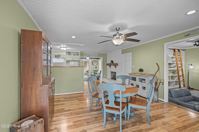 dining area with a fireplace, ornamental molding, light hardwood / wood-style floors, and ceiling fan