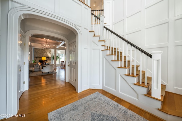 entrance foyer with arched walkways, a decorative wall, a chandelier, stairway, and light wood finished floors