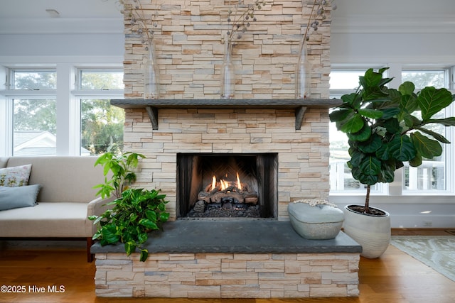 interior details featuring wood finished floors, ornamental molding, and a stone fireplace