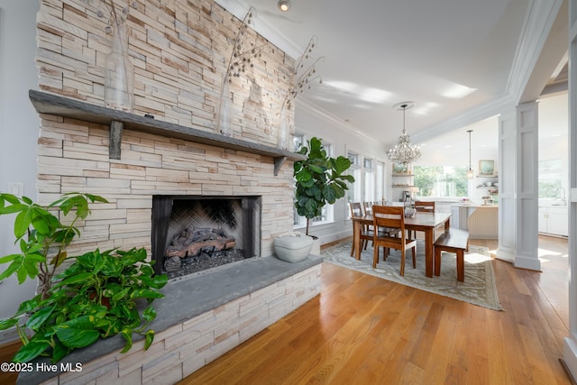 dining area featuring ornamental molding, a stone fireplace, a notable chandelier, and wood finished floors