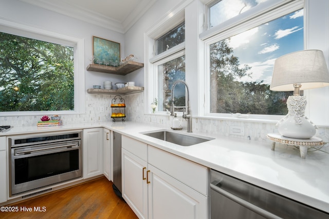 kitchen featuring appliances with stainless steel finishes, ornamental molding, white cabinetry, decorative backsplash, and a sink