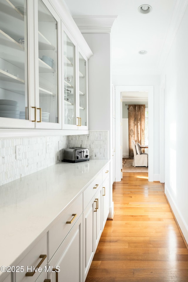 bar with tasteful backsplash, baseboards, light wood-style flooring, and crown molding