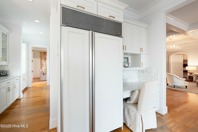 kitchen with built in fridge, arched walkways, crown molding, light wood finished floors, and white cabinetry