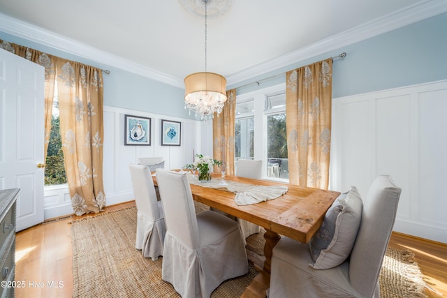 dining area featuring a chandelier, a decorative wall, light wood finished floors, and ornamental molding