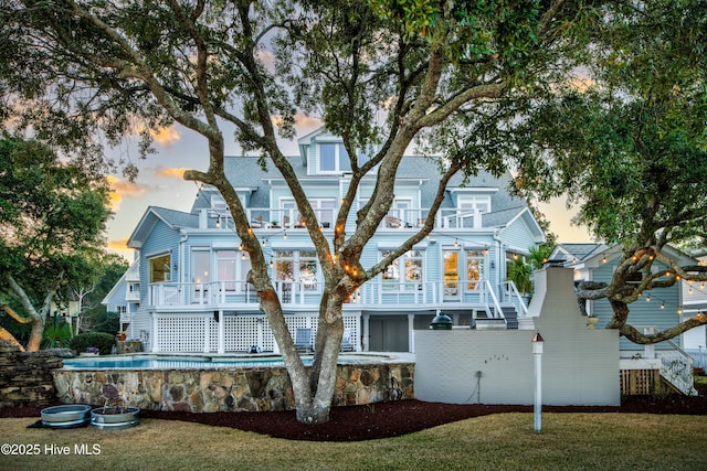 back house at dusk with a pool side deck, a lawn, and a balcony