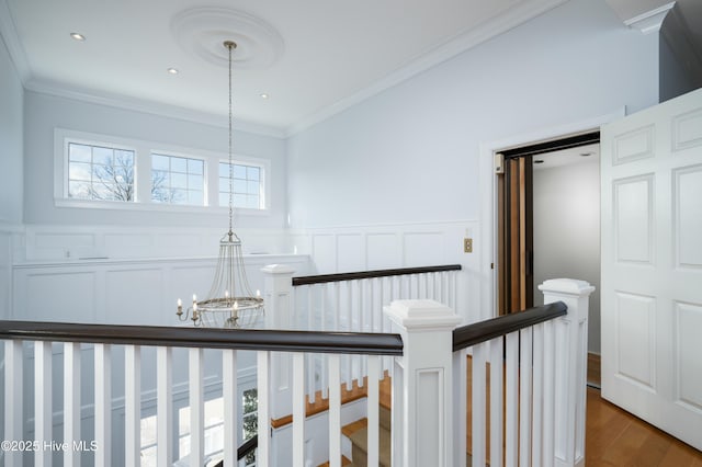 hall with crown molding, a notable chandelier, an upstairs landing, and a wainscoted wall