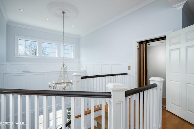 hallway with an inviting chandelier, dark wood-type flooring, ornamental molding, wainscoting, and an upstairs landing