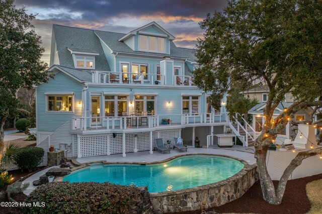 back of house at dusk featuring a yard, stairway, a balcony, and an outdoor pool