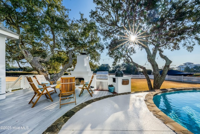 view of pool with a deck, an outdoor fireplace, fence, exterior kitchen, and grilling area