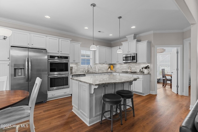 kitchen with sink, a kitchen island, pendant lighting, stainless steel appliances, and white cabinets