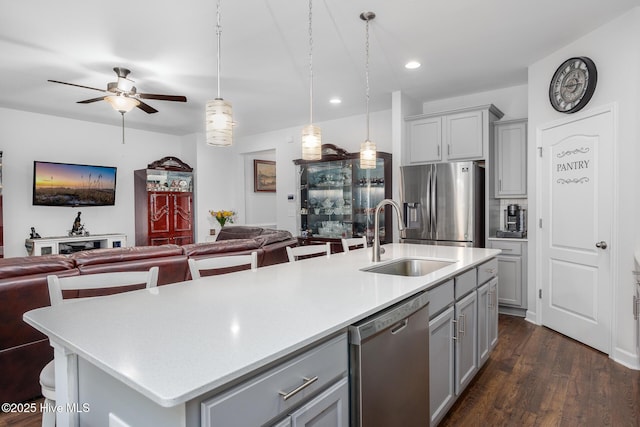 kitchen with pendant lighting, sink, gray cabinets, stainless steel appliances, and an island with sink