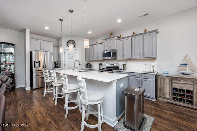 kitchen with sink, gray cabinetry, a center island with sink, pendant lighting, and stainless steel appliances