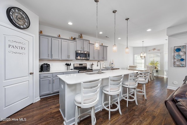 kitchen with sink, hanging light fixtures, appliances with stainless steel finishes, gray cabinets, and an island with sink