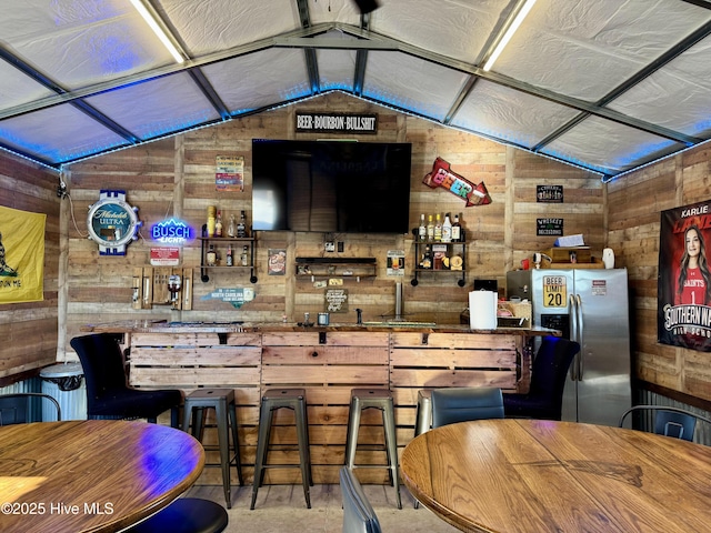 bar with vaulted ceiling, indoor bar, wood walls, and stainless steel fridge with ice dispenser