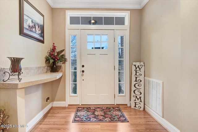 foyer entrance with visible vents, crown molding, and light wood finished floors