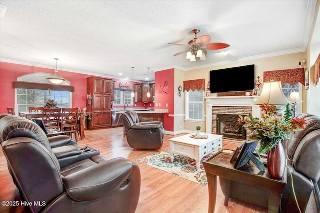 living room with a textured ceiling, a stone fireplace, light wood-style flooring, and crown molding