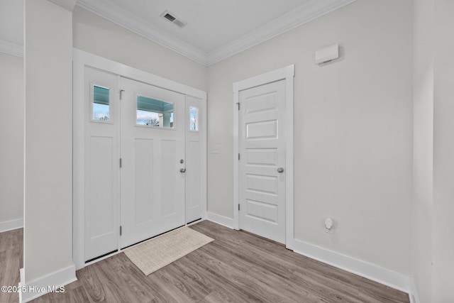 entryway with visible vents, wood finished floors, baseboards, and ornamental molding