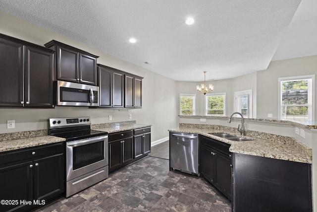 kitchen with sink, an inviting chandelier, light stone counters, hanging light fixtures, and appliances with stainless steel finishes