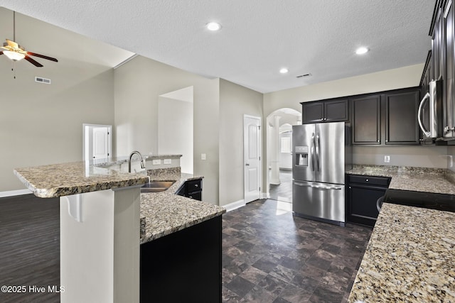 kitchen featuring sink, stainless steel fridge, a breakfast bar, light stone countertops, and a center island with sink