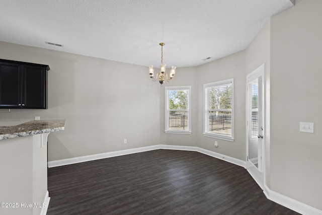 unfurnished dining area with a notable chandelier, dark wood-type flooring, and a textured ceiling