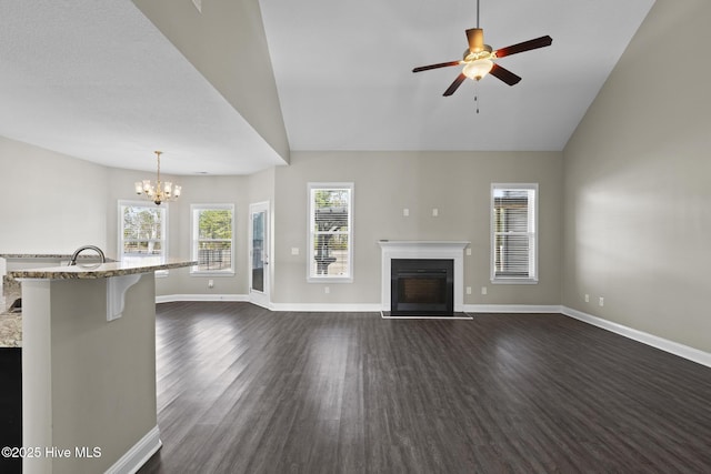 unfurnished living room with lofted ceiling, sink, ceiling fan with notable chandelier, and dark wood-type flooring