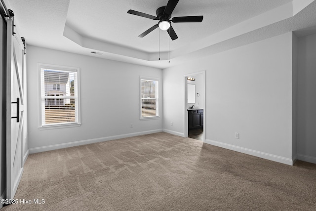 unfurnished bedroom with multiple windows, a tray ceiling, carpet floors, and a barn door