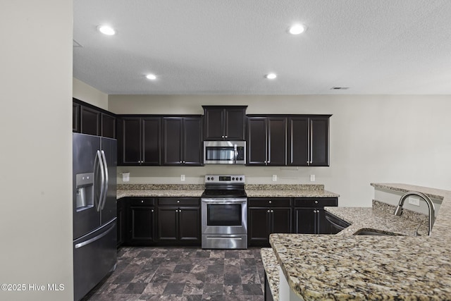 kitchen featuring light stone counters, sink, a textured ceiling, and appliances with stainless steel finishes