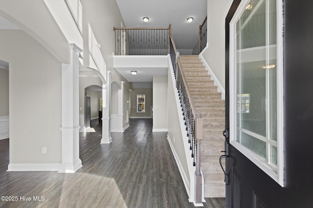 foyer entrance featuring ornate columns, a towering ceiling, and dark hardwood / wood-style flooring