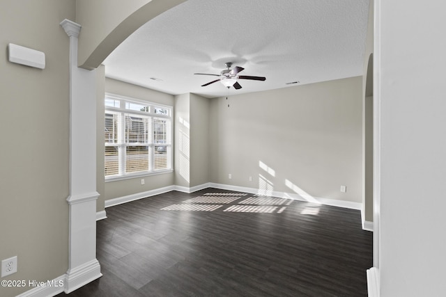 empty room with ceiling fan, dark hardwood / wood-style flooring, a textured ceiling, and ornate columns