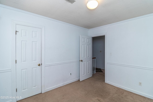 unfurnished bedroom with a textured ceiling, ornamental molding, baseboards, and light colored carpet