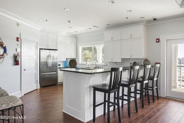 kitchen featuring dark wood-type flooring, stainless steel refrigerator, a breakfast bar, white cabinetry, and kitchen peninsula